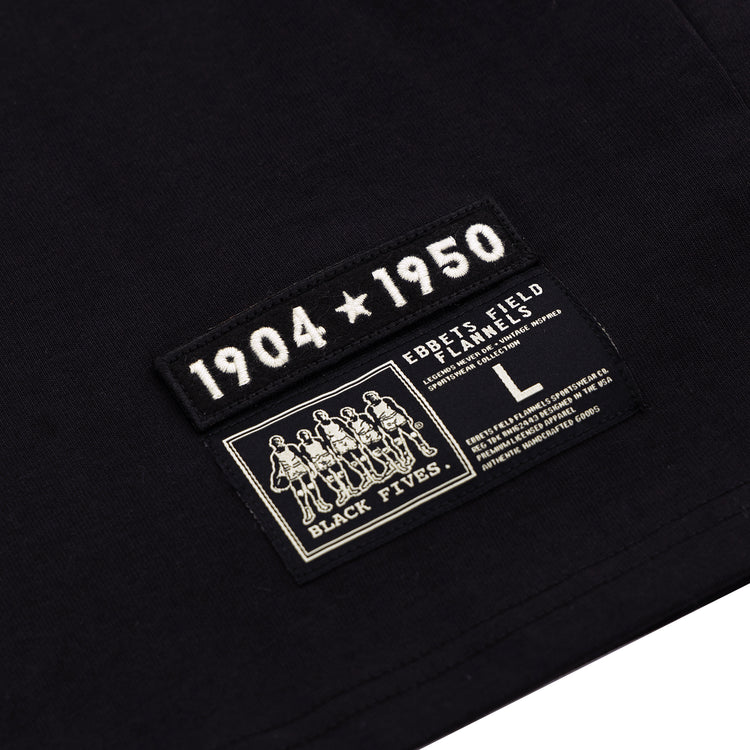 Close-up of a black fabric tag on the Black Fives T-Shirt by Ebbets Field Flannels, featuring “1904 ★ 1950” above the brand’s size L tag and an illustrated label honoring Black basketball history.