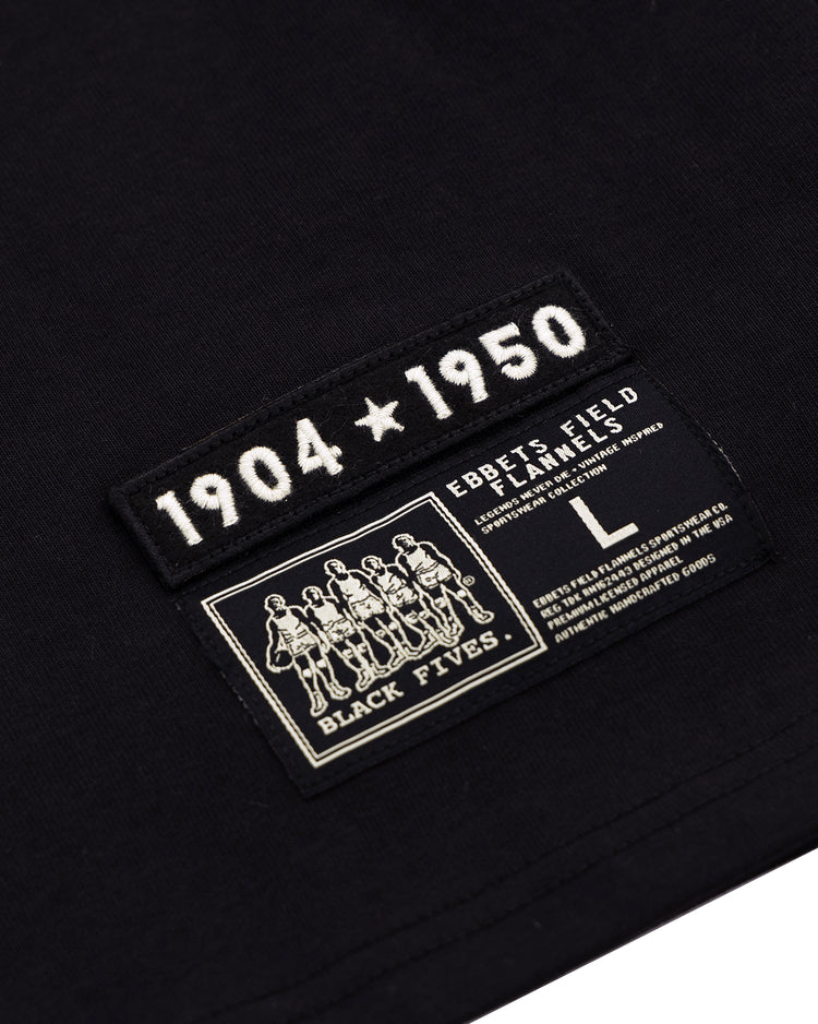 Close-up of a black fabric tag on the Black Fives T-Shirt by Ebbets Field Flannels, featuring “1904 ★ 1950” above the brand’s size L tag and an illustrated label honoring Black basketball history.