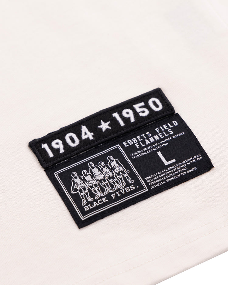A close-up of the Black Fives T-Shirt - White by Ebbets Field Flannels, size L, featuring two black patches: one reads 1904 ★ 1950, the other highlights Black basketball history with BLACK FIVES and care details.