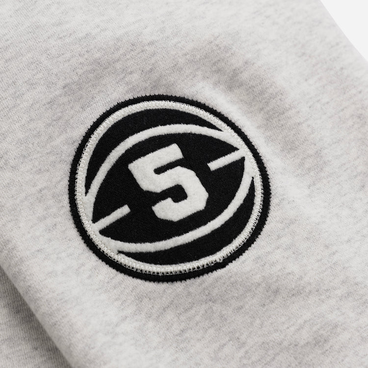 A close-up of the Black Fives Crewneck by EFF shows light gray fabric with a black circular patch, a white number 5 in the center, and curved lines—a tribute to Black basketball history.