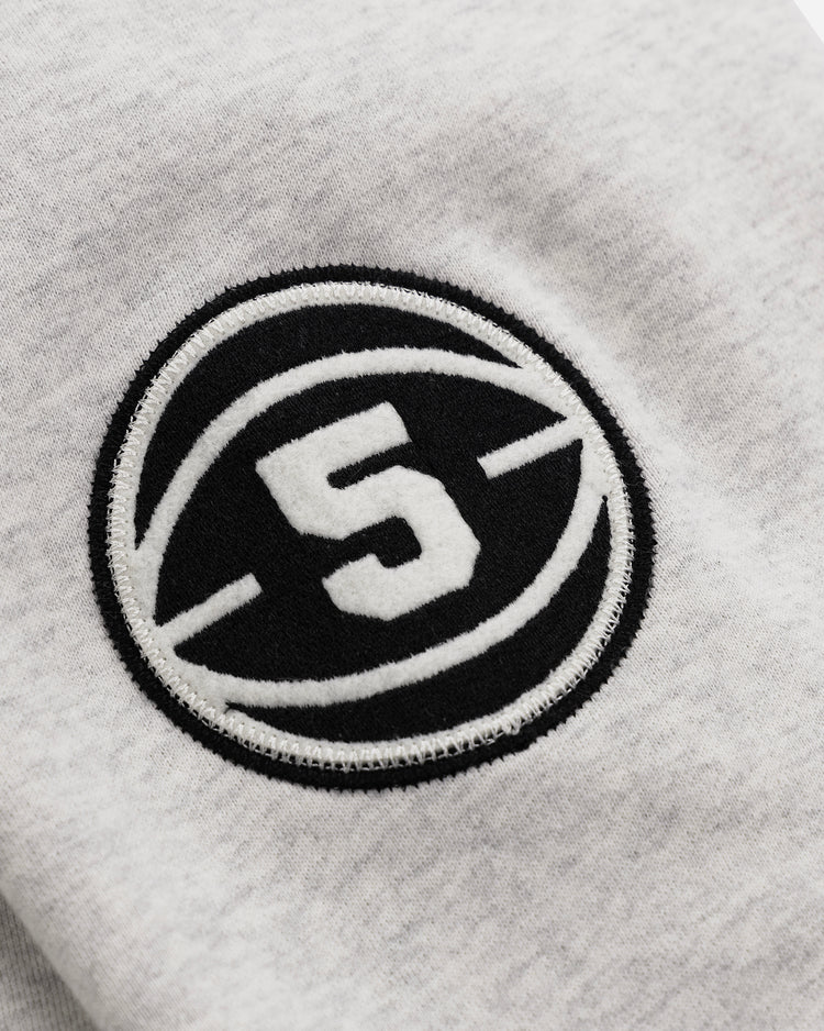 A close-up of the Black Fives Crewneck by EFF shows light gray fabric with a black circular patch, a white number 5 in the center, and curved lines—a tribute to Black basketball history.