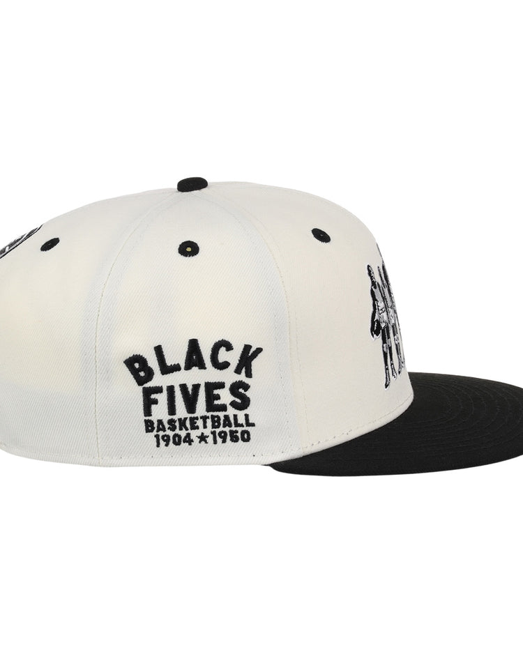 The Ebbets Field Flannels Black Fives Snapback Ballcap is a white and black cap with BLACK FIVES BASKETBALL 1904-1950 embroidered in black on the side, honoring Black basketball history. Features include a black brim and ventilation eyelets.