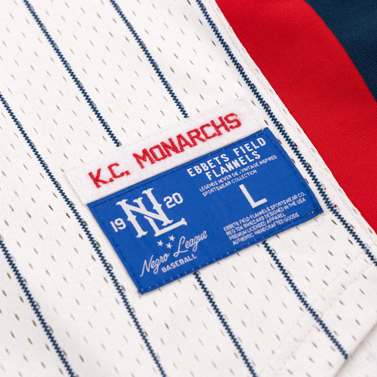 Close-up of the Kansas City Monarchs EFF NLB Pinstripe Button Down Jersey by EFF, showing a red K.C. MONARCHS patch and a blue Ebbets Field Flannels 1920 Negro National League label with sizing and care info.
