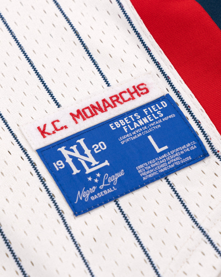 Close-up of the Kansas City Monarchs EFF NLB Pinstripe Button Down Jersey by EFF, showing a red K.C. MONARCHS patch and a blue Ebbets Field Flannels 1920 Negro National League label with sizing and care info.