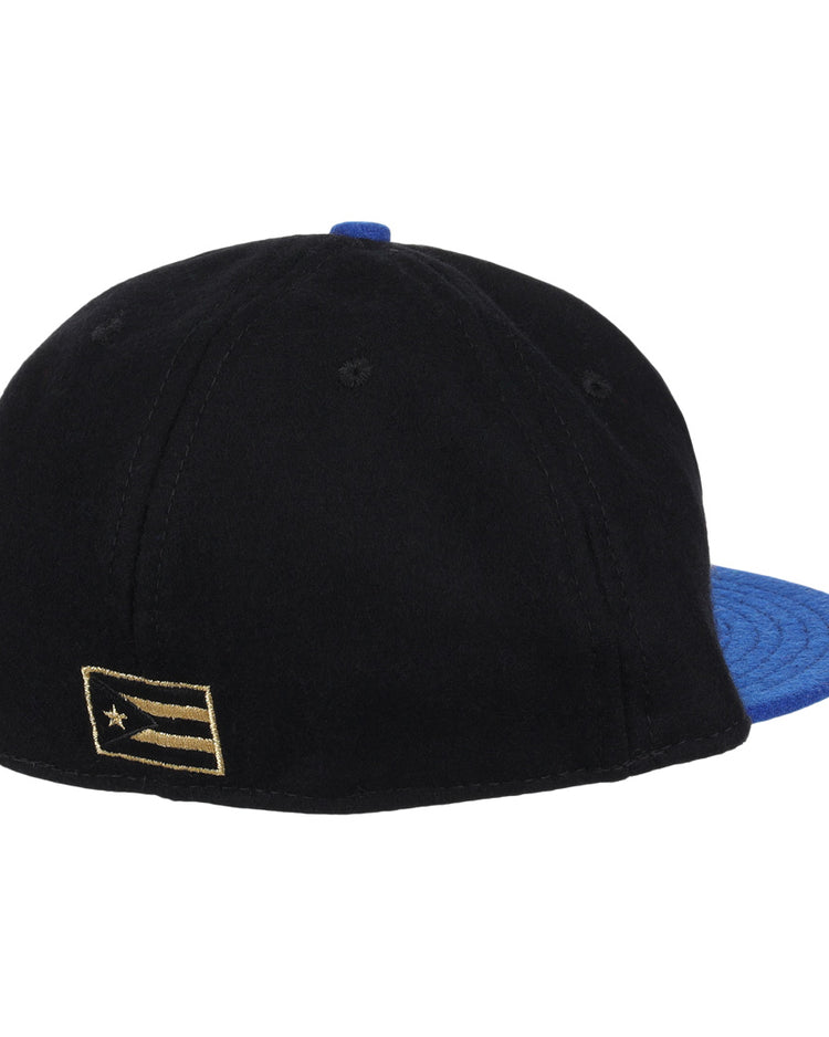 The EFF Santurce Cangrejeros Gilded Collection Ballcap in black features a blue brim and a gold-and-black flag patch on the left side, seen from the back—a stylish tribute to Puerto Rico League heritage.