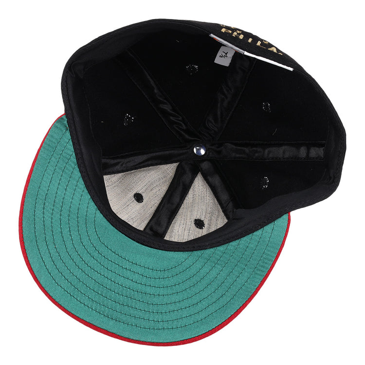 The EFF Philadelphia Stars Gilded Collection Ballcap is flipped upside down to reveal its green underside brim with red trim, black interior panels, blue center button, and a visible size tag—ideal for any Negro National League collector.