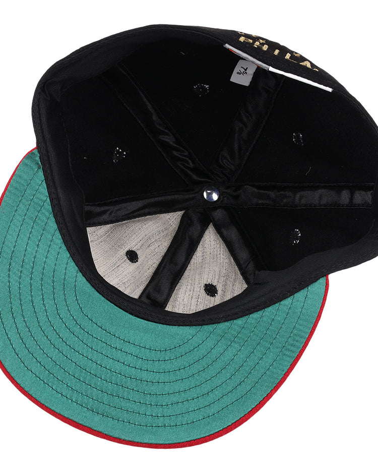 The EFF Philadelphia Stars Gilded Collection Ballcap is flipped upside down to reveal its green underside brim with red trim, black interior panels, blue center button, and a visible size tag—ideal for any Negro National League collector.