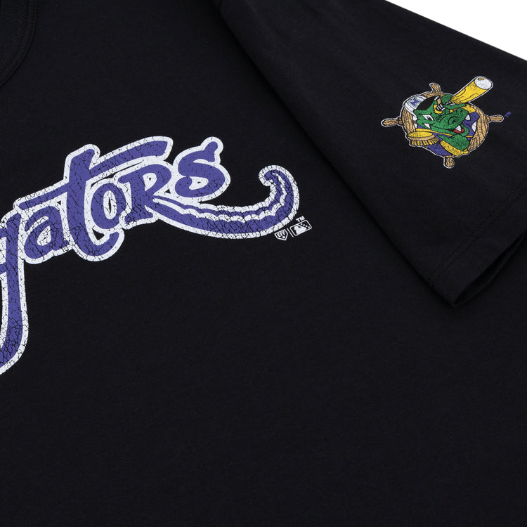 Close-up of the black Norwich Navigators EFF MiLB Vintage T-Shirt by Ebbets Field Flannels, featuring “Gators” in purple and white script on the front and a small cartoon alligator swinging a bat on the sleeve.