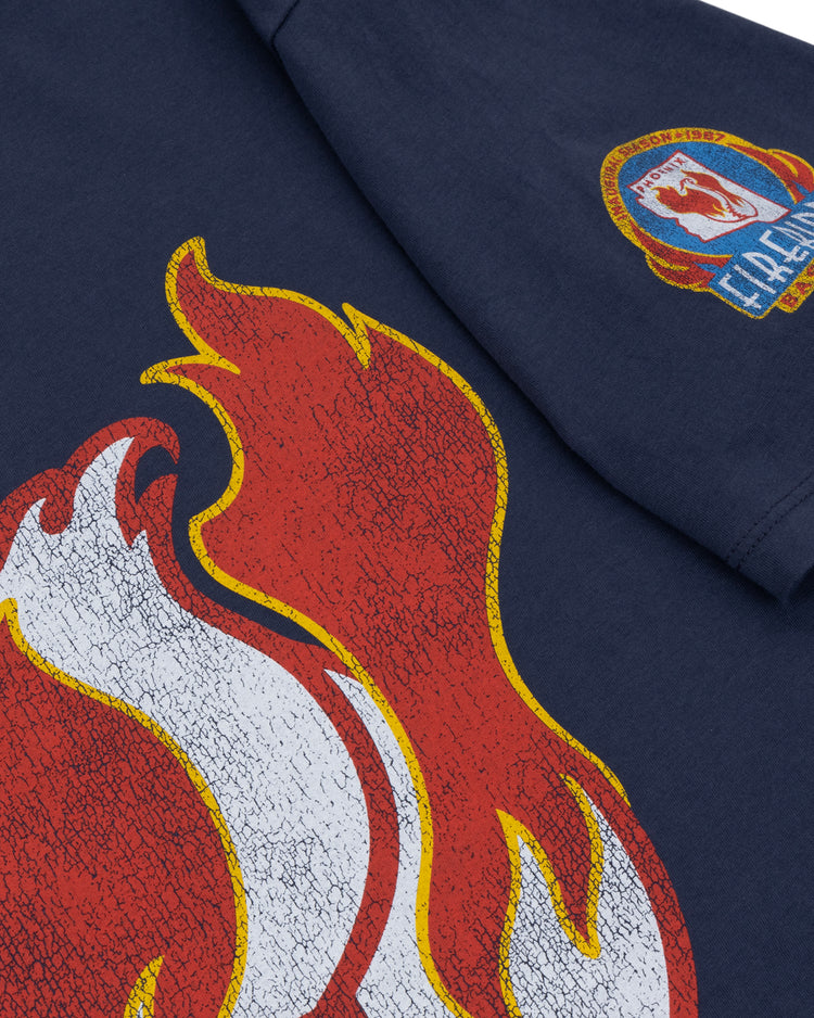 The Ebbets Field Flannels Phoenix Firebirds EFF MiLB Vintage T-Shirt features a navy blue design with a bold red and white flame graphic and a colorful Fireland patch on the sleeve, inspired by classic Minor League styles.