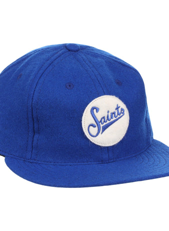 The EFF St. Paul Saints Letterhead Wool Vintage Ballcap is a blue wool cap with a flat brim and a white circular patch on the front that displays Saints in blue cursive, inspired by classic Minor League logos.
