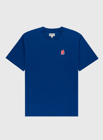 The Ebbets Field Los Angeles Angels (PCL) Embroidered ‘LA’ Short Sleeve Tee features a plain blue design with a small red and white 1942 LA team logo on the left chest, shown on a light gray background.