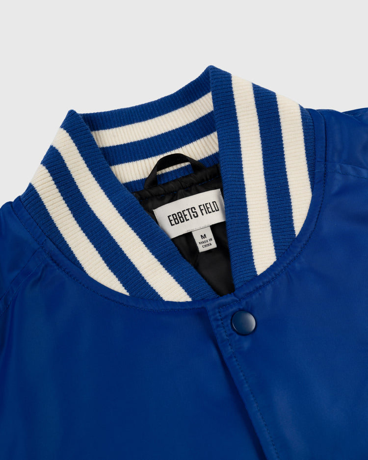 A close-up of a royal blue Los Angeles Angels (PCL) Satin Varsity Jacket by Ebbets Field, featuring a white and blue striped ribbed collar, snap buttons, and an Ebbets Field size M label, inspired by classic minor league baseball jackets.