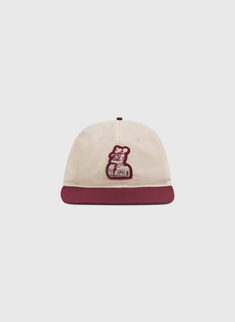 The Texas A&M Sarge Cotton Twill Ballcap by Ebbets Field is a cream-colored cap with a maroon brim, featuring an embroidered graphic of a person holding a dog on the front—an ideal choice for Texas A&M University fans looking for stylish comfort.