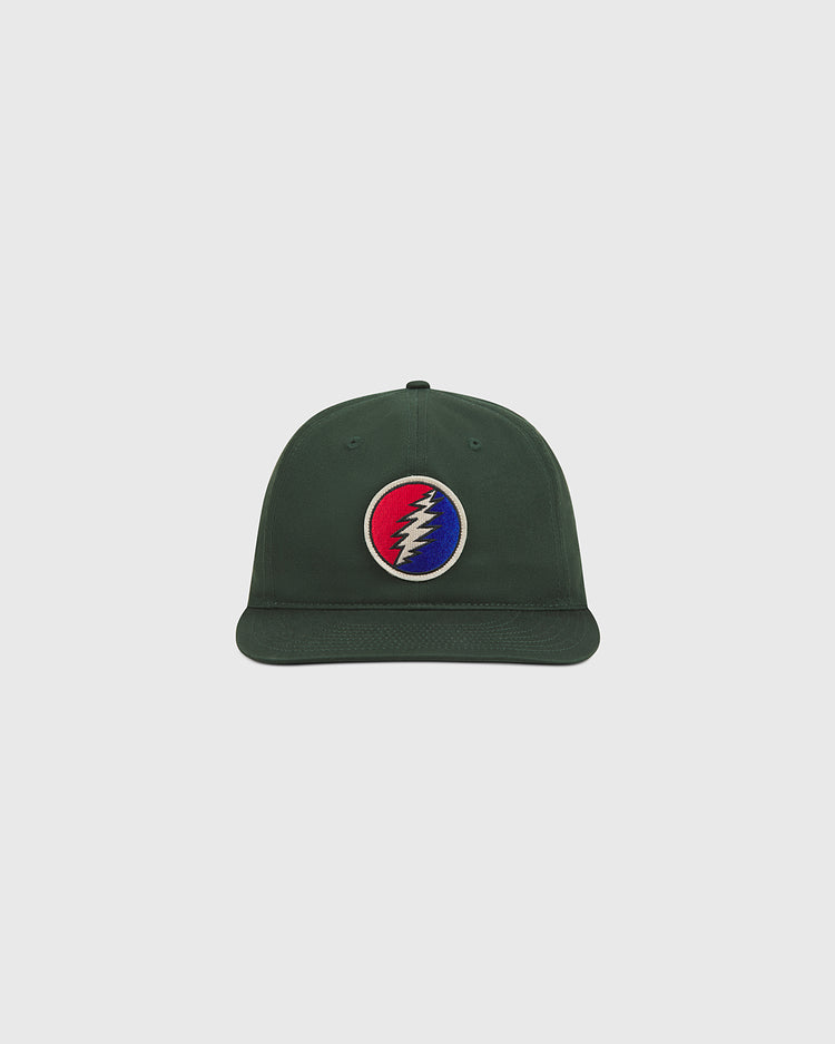 The Ebbets Field Grateful Dead Lightning Bolt Cotton Twill Ballcap is a dark green hat featuring a circular patch with a red, white, and blue lightning bolt logo on the front, displayed against a plain light gray background.