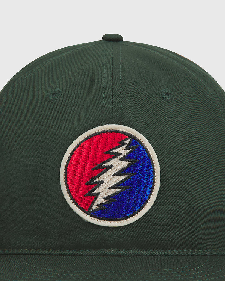 The Grateful Dead Lightning Bolt Cotton Twill Ballcap by Ebbets Field is a dark green hat made from cotton twill, featuring a circular front patch with a red and blue background divided by a white lightning bolt logo outlined in white—a classic accessory for Grateful Dead fans.