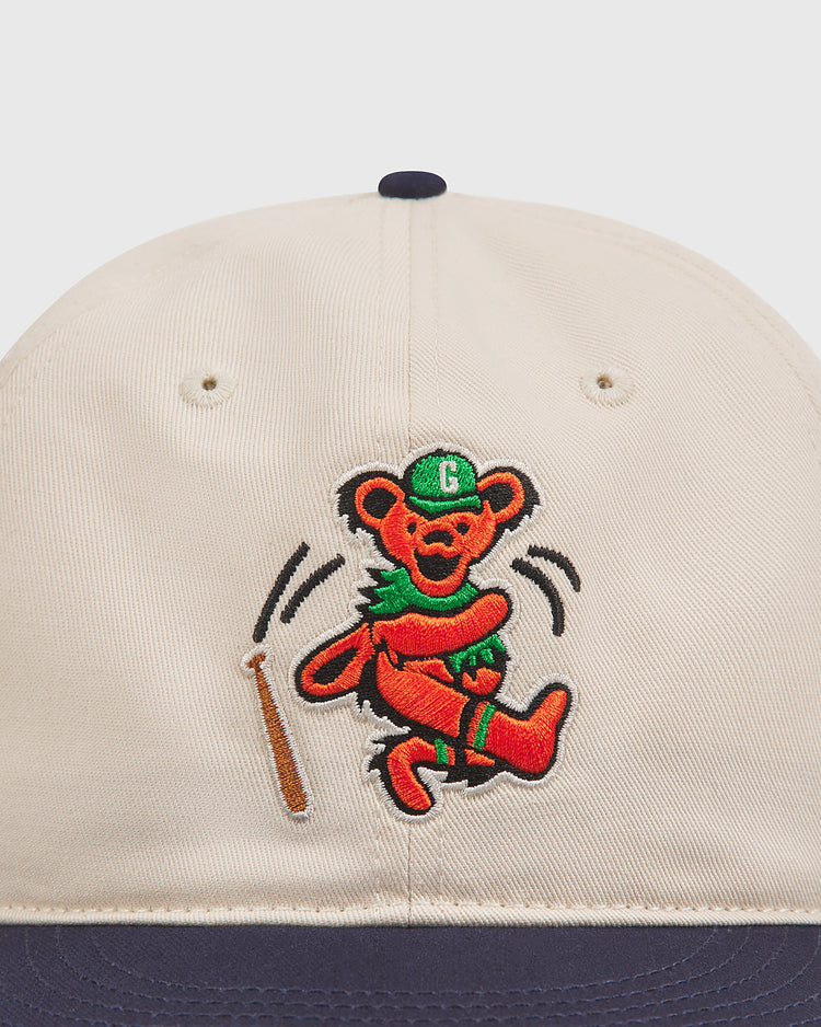 The Ebbets Field Grateful Dead Baseball Bear Cotton Twill Ballcap features a beige and navy design with an embroidered bear sporting a green cap and scarf, dancing beside a brown baseball bat. This playful ballcap brings a fun Grateful Dead-inspired flair to any casual ensemble.