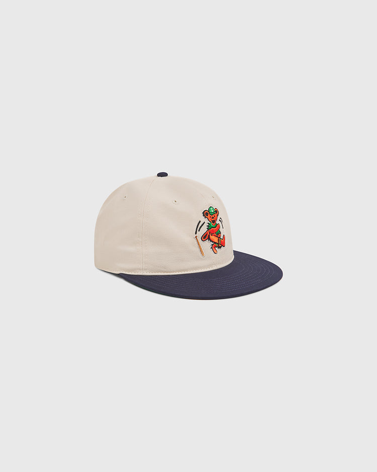 Introducing the Grateful Dead Baseball Bear Cotton Twill Ballcap by Ebbets Field—a cream-colored cotton twill hat with a navy blue brim, showcasing a small embroidered cartoon graphic of an orange bear running, set against a plain light background. Perfect for fans looking for a playful twist on the classic Grateful Dead ballcap style.