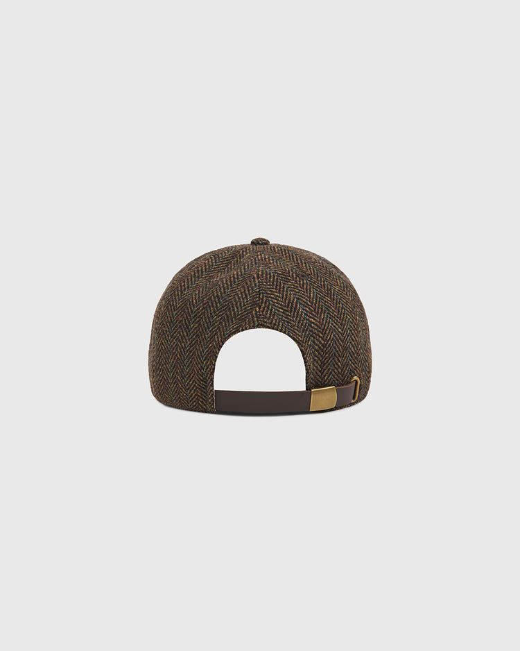 The Ebbets Field Harvard University Herringbone Wool Ballcap, shown from the back, displays its brown herringbone pattern and features an adjustable strap with a metallic buckle. The cap is set against a plain light gray background.