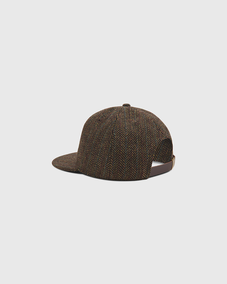 The Harvard University Herringbone Wool Ballcap by Ebbets Field is shown from the back and slightly to the side, highlighting its brown herringbone pattern, flat brim, and adjustable strap. This stylish cap stands out against a plain light gray background.