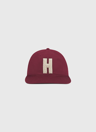 The Ebbets Field Harvard University Chenille H Cotton Twill Ballcap, featuring a maroon design with an oversized beige chenille “H” on the front, is displayed against a plain light gray background.