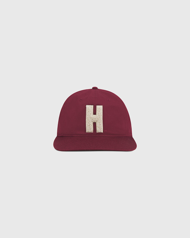 The Ebbets Field Harvard University Chenille H Cotton Twill Ballcap, featuring a maroon design with an oversized beige chenille “H” on the front, is displayed against a plain light gray background.
