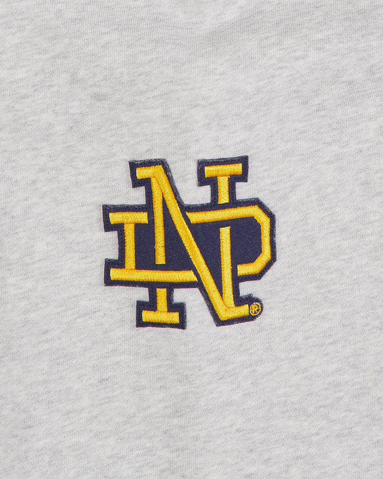 A yellow and navy blue interlocking N and P logo is embroidered on light gray fabric, adding a subtle nod to Irish heritage hoodie style, is rewritten as: The Ebbets Field Notre Dame X Guinness Heavyweight Pullover Hoodie features an embroidered yellow and navy blue interlocking N and P logo on light gray fabric, giving a subtle nod to Irish heritage style.