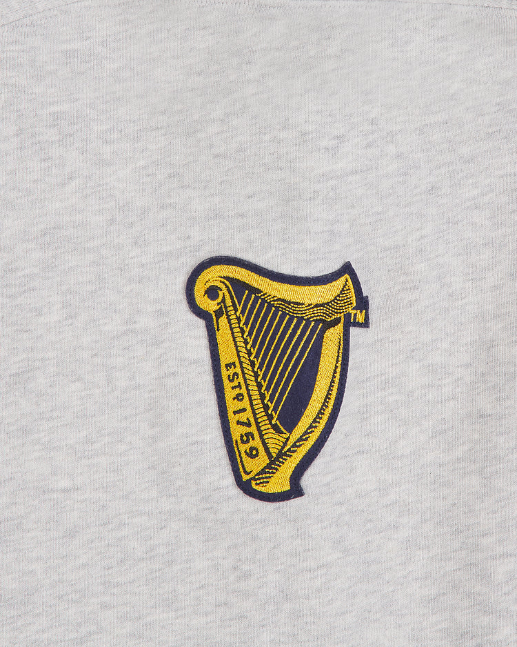 A gold harp logo outlined in black with the text ESTD 1759 is embroidered on light gray fabric, giving the Ebbets Field Notre Dame X Guinness Heavyweight Pullover Hoodie a classic touch.