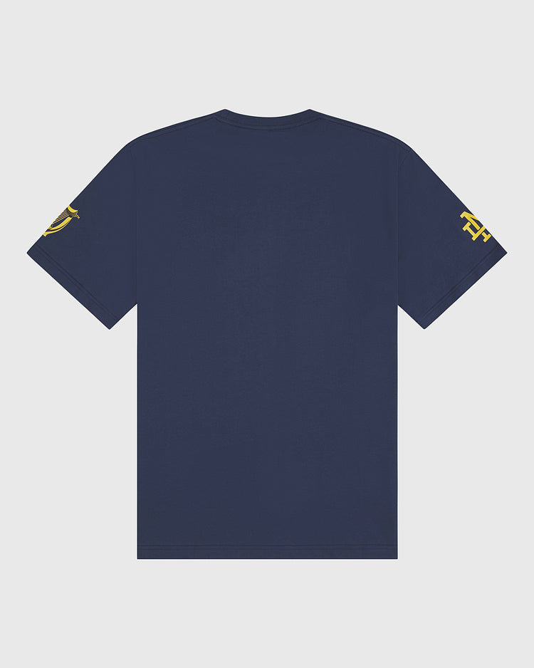A plain navy blue Notre Dame X Guinness Short Sleeve Graphic Tee by Ebbets Field is shown from the back, featuring yellow graphic designs on both sleeves. Reminiscent of vintage Irish heritage t-shirts, this style stands out against a light gray background.