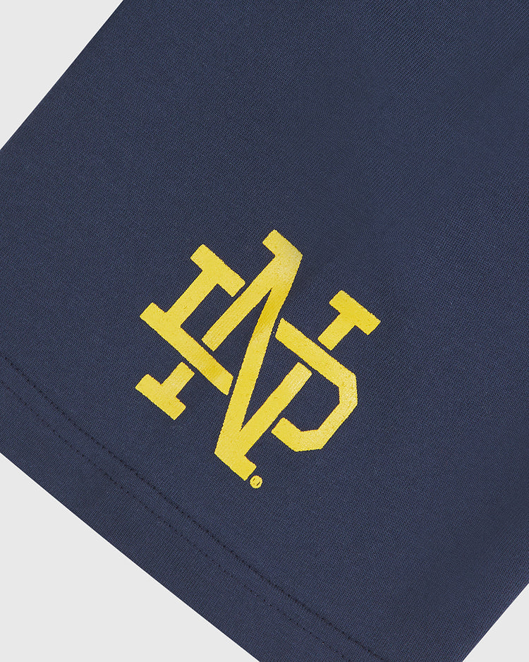 Crafted by Ebbets Field, the Notre Dame X Guinness Short Sleeve Graphic Tee features navy blue fabric adorned with a yellow interlocking ND monogram logo printed near the edge—evoking the timeless style of classic Notre Dame Guinness shirts and vintage tees that celebrate Irish heritage.