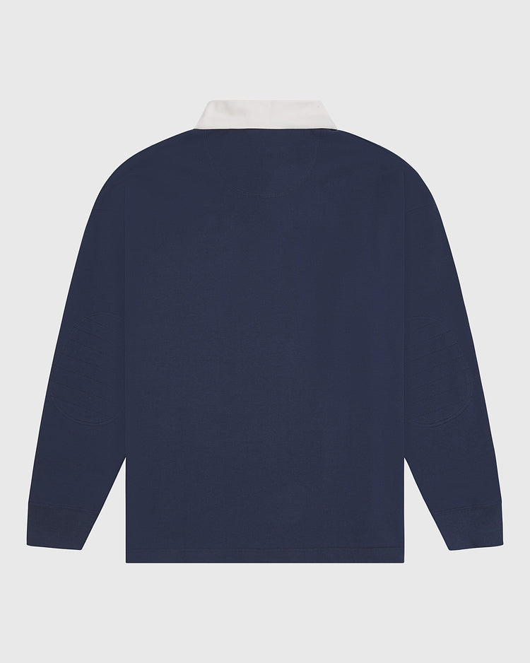 The Ebbets Field Notre Dame X Guinness Rugby Shirt is displayed flat, showing the back view. This navy blue long-sleeve shirt features a white collar and ribbed cuffs, drawing inspiration from classic Irish heritage. The design is plain with no visible patterns or logos.