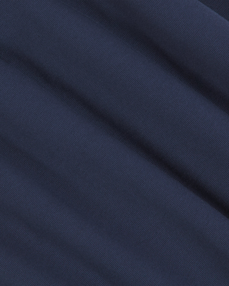 Close-up view of deep blue fabric with gentle, diagonal folds and a subtly ribbed texture, reminiscent of the premium materials featured in the Notre Dame X Guinness Rugby Shirt by Ebbets Field. The smooth, uniform color of the material evokes a subtle sense of Irish heritage.