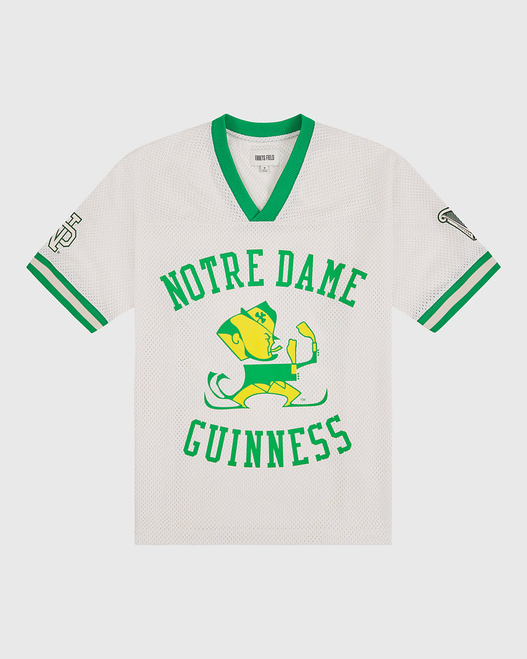 Show your Irish pride with the Notre Dame X Guinness Mesh Football Jersey by Ebbets Field. This white mesh sports jersey features green trim, a leprechaun mascot holding a beer, and the words “Notre Dame Guinness” in green across the front. Designed with classic symbols on both sleeves, this vintage-inspired football jersey is perfect for fans who appreciate tradition and want to celebrate their Irish heritage in authentic Ebbets Field style.
