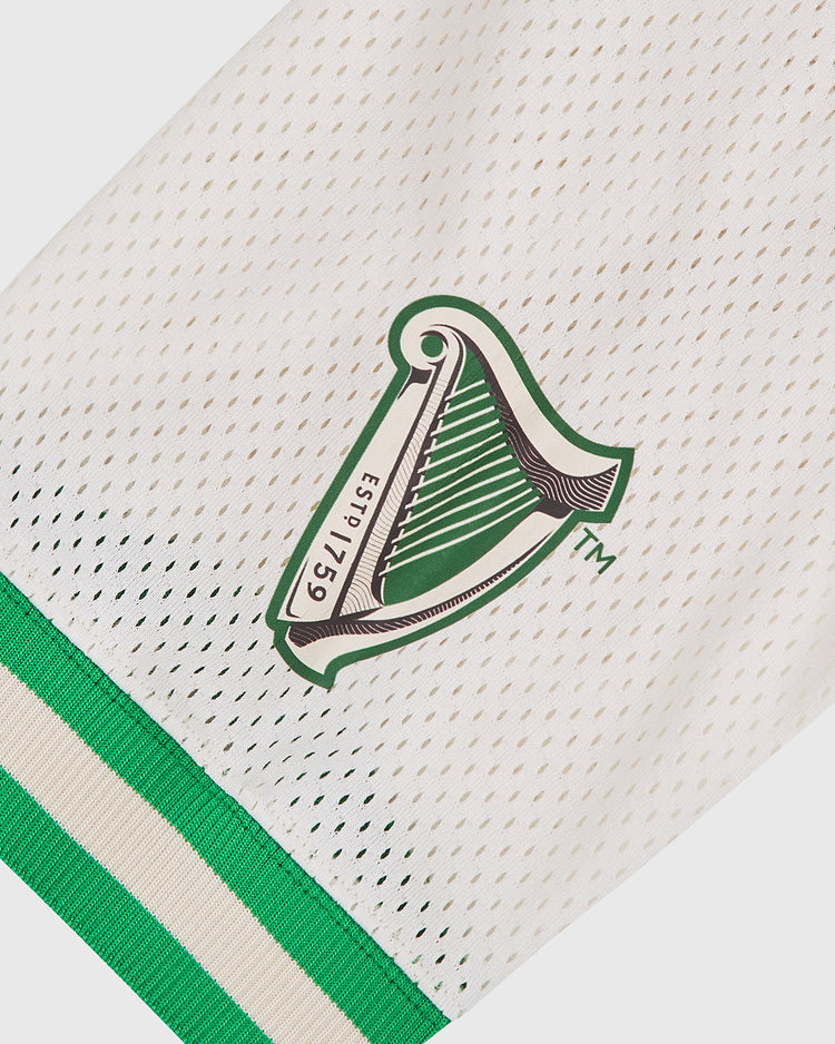 Close-up of the Notre Dame X Guinness Mesh Football Jersey by Ebbets Field, featuring a white mesh fabric with a green harp logo labeled “Estb 1759” and green and beige striped trim at the edge, evoking the classic style of a vintage football jersey.
