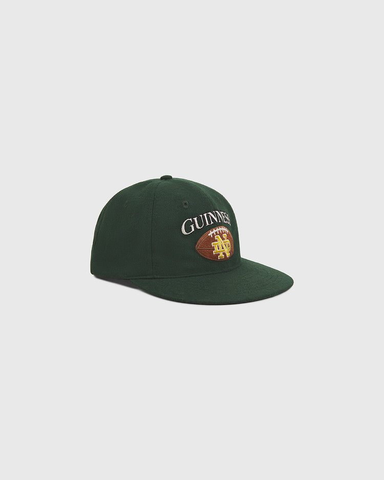 A Notre Dame X Guinness Wool Ballcap by Ebbets Field, featuring dark green wool and an embroidered Guinness and football logo on the front, displayed against a plain white background.