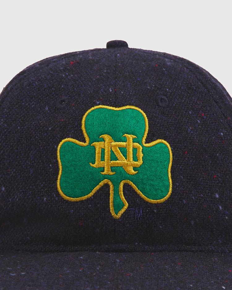 Introducing the Ebbets Field Notre Dame X Magee Irish Donegal Wool Ballcap—a dark wool cap showcasing a green shamrock outlined in yellow with interlocking yellow N and D embroidery on the front. This classic ballcap blends heritage and team pride for an authentic, timeless look.