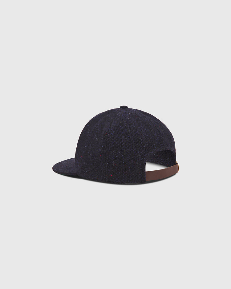 The Ebbets Field Notre Dame X Magee Irish Donegal Wool Ballcap, crafted from dark blue Donegal wool and featuring a brown adjustable strap at the back, is displayed against a plain light gray background.