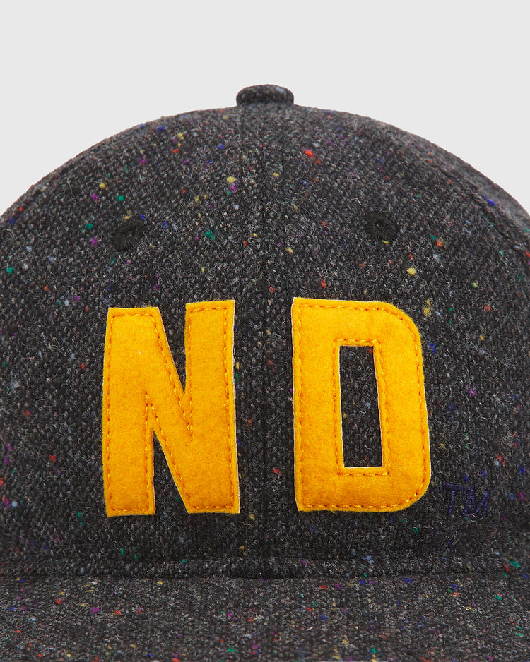 A close-up of the Ebbets Field Notre Dame X Magee Irish Donegal Wool Ballcap, crafted from dark grey speckled fabric reminiscent of classic Irish wool hats, featuring large yellow “ND” embroidered on the front.