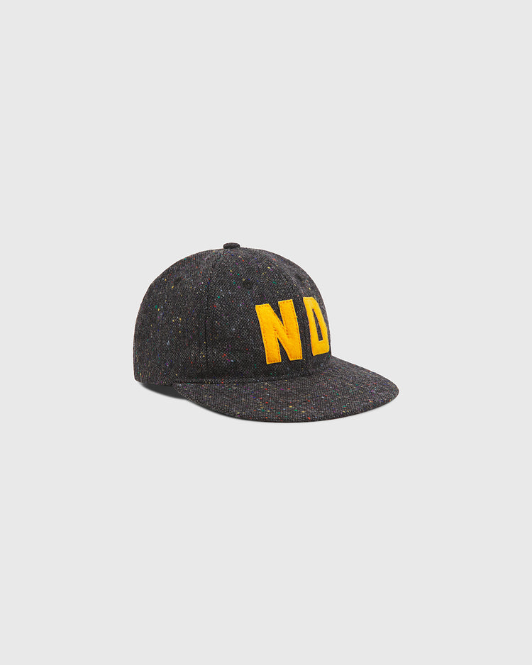 The Notre Dame X Magee Irish Donegal Wool Ballcap by Ebbets Field is a dark gray baseball cap made from speckled fabric inspired by traditional Donegal wool ballcap styles, featuring bold yellow “ND” embroidery on the front, shown against a plain light gray background.