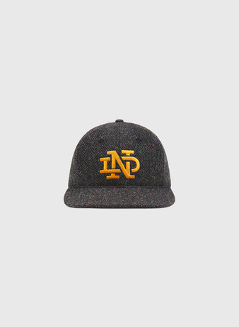 The Notre Dame X Magee Irish Donegal Wool Ballcap by Ebbets Field features a dark gray textured Donegal wool construction with a yellow embroidered ND logo on the front, shown against a plain light gray background.