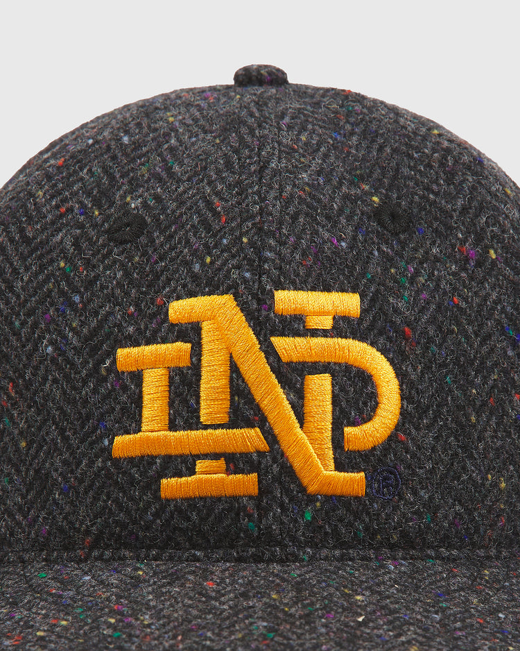 A close-up of the Ebbets Field Notre Dame X Magee Irish Donegal Wool Ballcap, crafted from dark speckled Donegal wool and featuring a prominent yellow ND logo embroidered on the front.