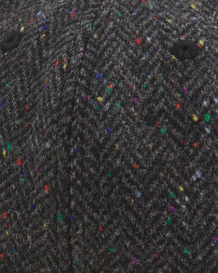 Close-up of the Notre Dame X Magee Irish Donegal Wool Ballcap by Ebbets Field, highlighting the textured dark gray Donegal wool with a classic herringbone pattern and multicolored flecks in red, yellow, blue, green, and purple. Two small black stitched eyelets are also visible.