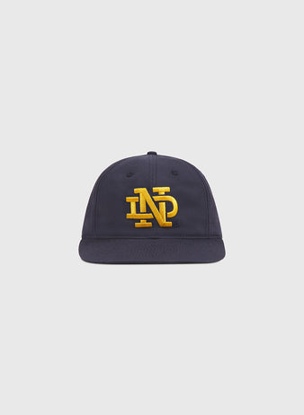 The Ebbets Field Notre Dame Cotton Ballcap is a navy blue baseball cap with a flat brim, featuring large yellow embroidered “NP” letters on the front, displayed on a plain light background.