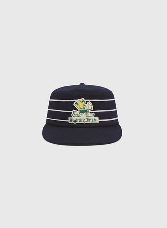 The Ebbets Field Notre Dame Pillbox Cap is a navy blue hat with white horizontal stripes and a leprechaun-adorned Fighting Irish logo on the front, displayed against a plain light gray background.
