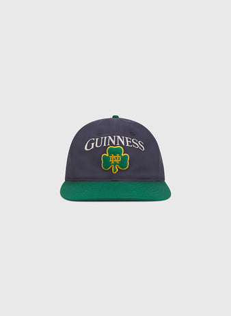 Show your Irish pride in style with the Notre Dame X Guinness Cotton Ballcap by Ebbets Field. This navy blue hat features a green brim, and displays “GUINNESS” above a green shamrock with yellow trim on the front—an ideal choice for celebrating your heritage or elevating your cap collection.