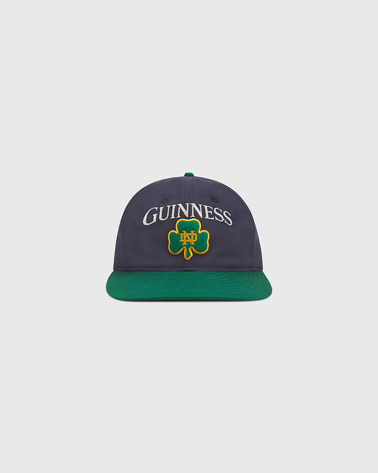 Show your Irish pride in style with the Notre Dame X Guinness Cotton Ballcap by Ebbets Field. This navy blue hat features a green brim, and displays “GUINNESS” above a green shamrock with yellow trim on the front—an ideal choice for celebrating your heritage or elevating your cap collection.