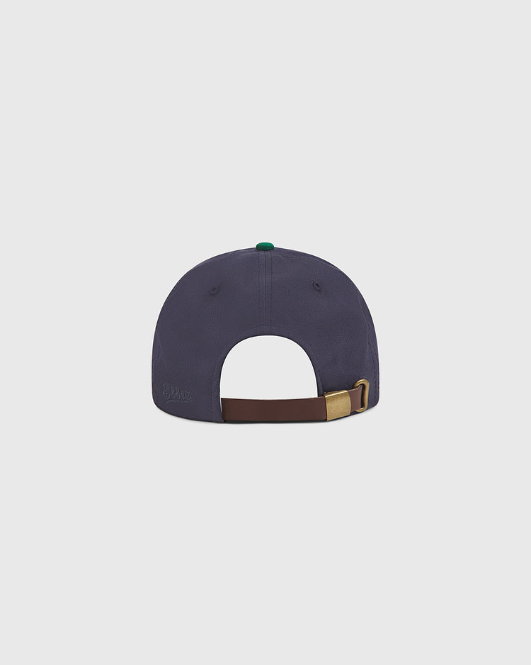 A navy blue Notre Dame X Guinness Cotton Ballcap by Ebbets Field is shown from the back, featuring a brown adjustable strap with a gold buckle. This classic hat stands out against a plain light gray background.