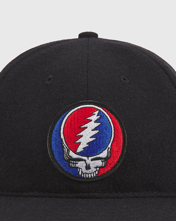 The Grateful Dead Stealie Wool Ballcap by Ebbets Field is a black wool ballcap featuring a circular patch with a skull and red, white, and blue lightning bolt design inspired by the iconic Grateful Dead Stealie logo.
