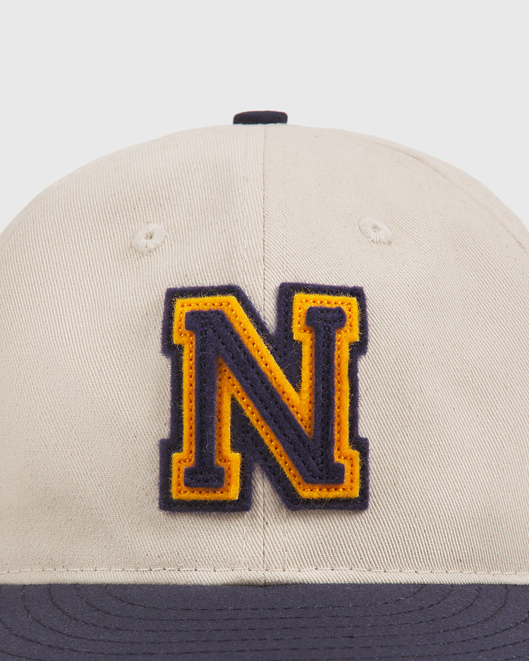 A beige Ebbets Field Navy 1958 Logo Cotton Twill Ballcap featuring a prominent yellow and black “N” patch on the front and a dark blue brim.