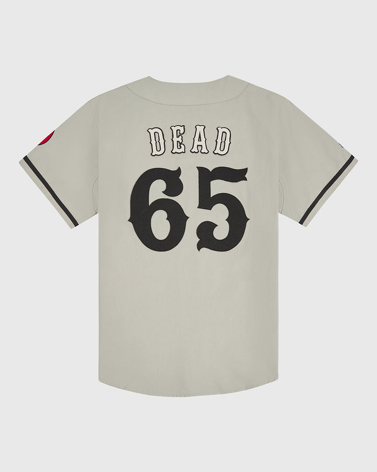 This Grateful Dead Cotton Twill Button-Up Baseball Jersey by Ebbets Field features a light gray twill fabric with “DEAD” and the number 65 boldly displayed in large black letters on the back. Black trim accents the sleeves, while a red patch on the left arm adds an extra pop, making this an eye-catching piece of psychedelic band apparel.