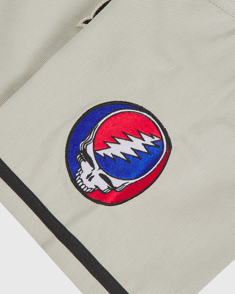 The Ebbets Field Grateful Dead Cotton Twill Button-Up Baseball Jersey features a circular patch showcasing a skull and red and blue lightning bolt design outlined in black—a must-have for fans of psychedelic band apparel.